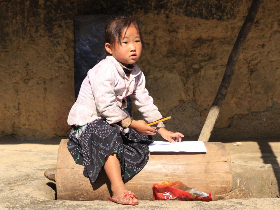Lokaal Thai-meisje kijkt op van haar schrift in Ha Giang