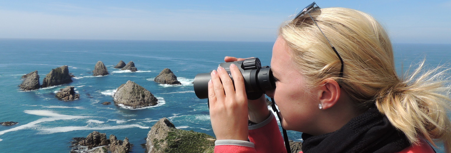 Door een verrekijker tuurt Van Verre medewerker Astrid voor een nog mooier uitzicht bij Nugget Point, Nieuw-Zeeland