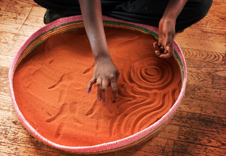 Een aboriginal maakt prachtige zandtekeningen in de omgeving van Uluru, Australië