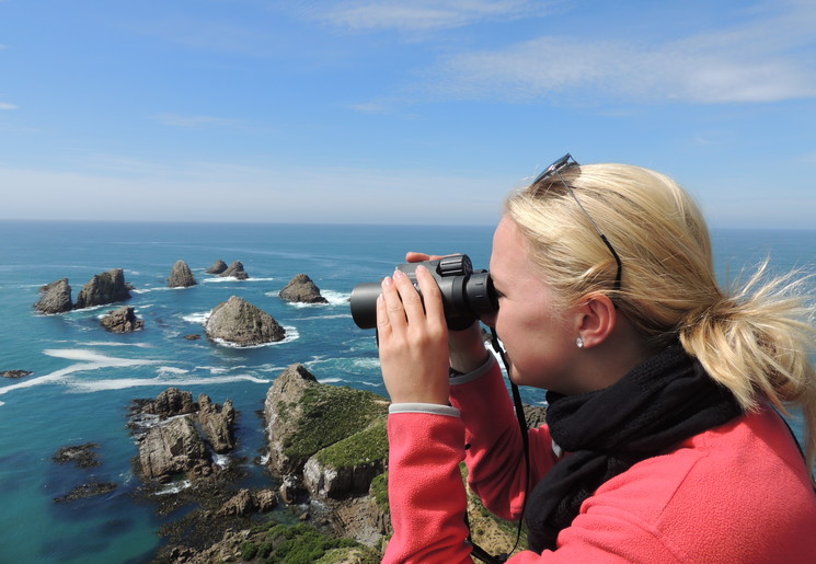 Door een verrekijker tuurt Van Verre medewerker Astrid voor een nog mooier uitzicht bij Nugget Point, Nieuw-Zeeland Door een verrekijker tuurt Van Verre medewerker Astrid voor een nog mooier uitzicht bij Nugget Point, Nieuw-Zeeland