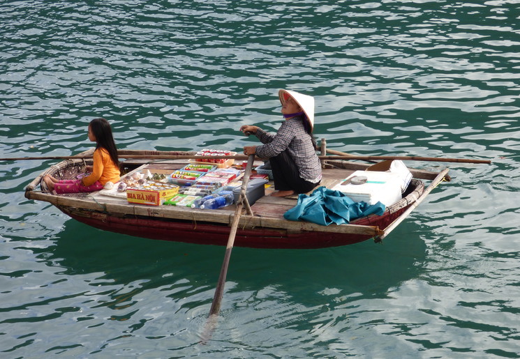 De kleine supermarktbootjes varen tussen de grote schepen in Bai Tu Long, Vietnam