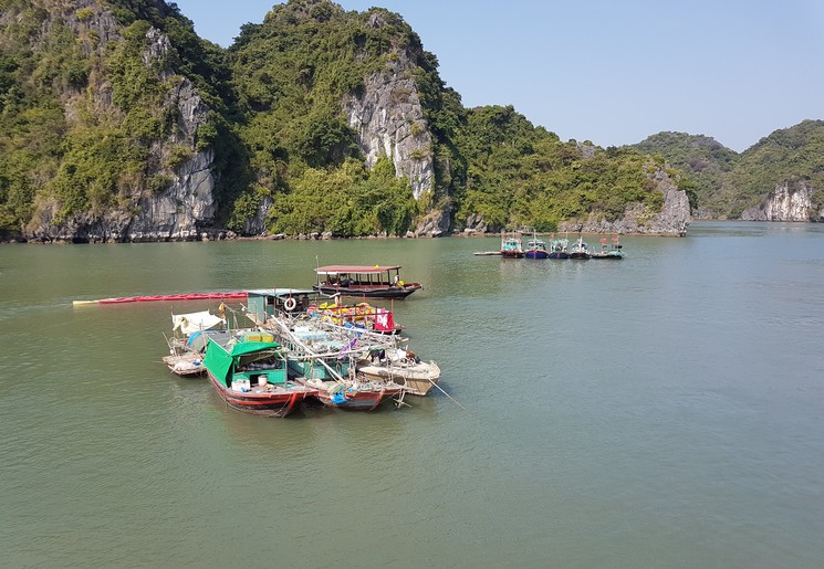 Lokale bootjes met goederen drijven voor het karstlandschap van Halong Bay, Vietnam
