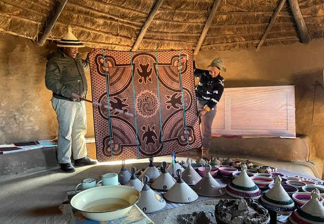 Inwoners van Lesotho tonen handgemaakte kleden en traditioneel aardewerk in een Basotho-hut